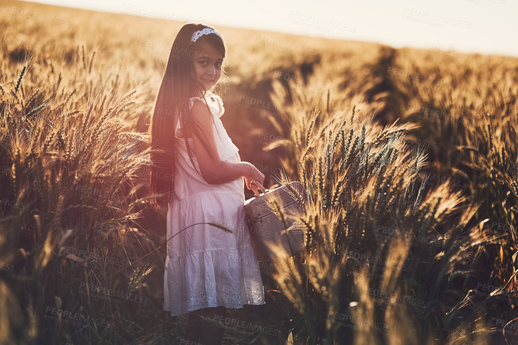 Buy stock photo Portrait, child and smile for adventure in countryside, nature and playing in cornfield with suitcase. Outdoor, girl and walking in holiday, spring and freedom in environment, farm and vacation