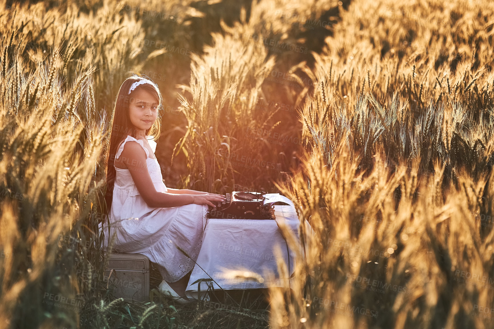 Buy stock photo Girl, field and typewriter for story and nature, portrait and vintage writing equipment. Typing, author or young child person on farm in Texas for relax, sunshine and summer with table or antique