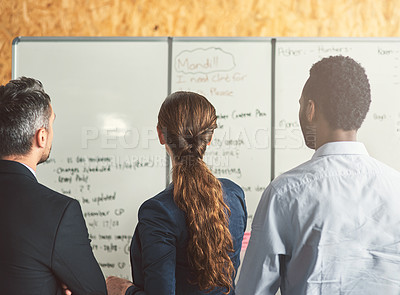 Buy stock photo Rearview shot of young businesspeople discussing ideas on a whiteboard during a meeting in an office