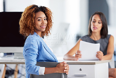 Buy stock photo Portrait of two smiling young businesswomen sitting together at a desk in an office