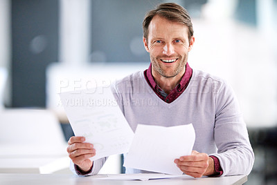 Buy stock photo Portrait of a mature businessman reading paperwork while sitting in an office