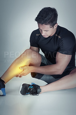 Buy stock photo Studio shot of an athletic young man holding his leg in pain against a grey background