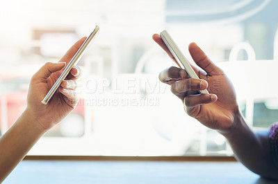 Buy stock photo Shot of two unidentifiable friends using their smartphones together