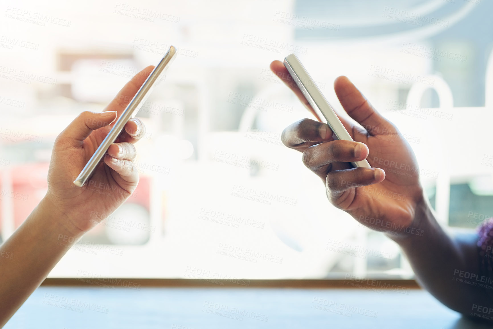 Buy stock photo Shot of two unidentifiable friends using their smartphones together