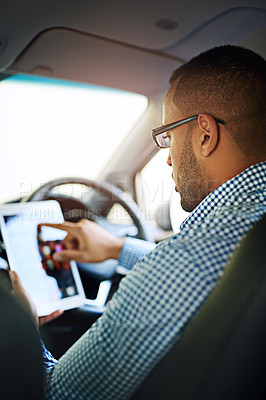 Buy stock photo Cropped shot of a young businessman using a digital tablet while driving a car