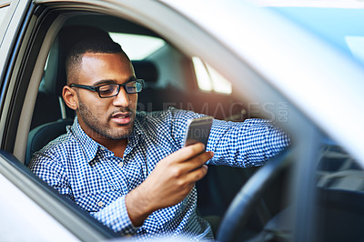 Buy stock photo Cropped shot of a young businessman using a cellphone while driving a car