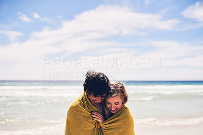 Buy stock photo Cropped shot of an affectionate young couple wrapped in a blanket on the beach