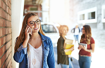 Buy stock photo Shot of a smiling female university student standing on campus talking a cellphone with friends in the background