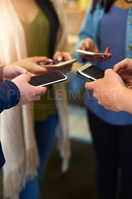 Buy stock photo Shot of a group of unidentifiable friends using their smartphones together