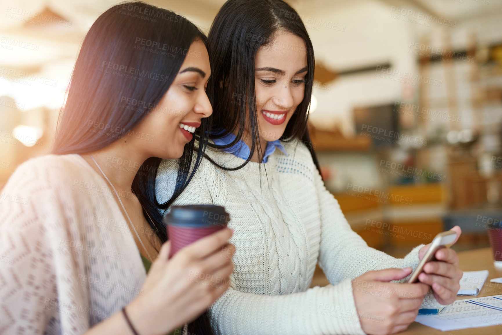Buy stock photo Shot of two young students using a smartphone while studying together in a cafe