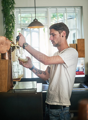 Buy stock photo Shot of a young bartender pouring beer from a tap behind the bar
