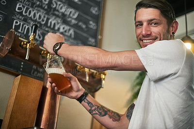 Buy stock photo Portrait of a young bartender pouring beer from a tap behind the bar
