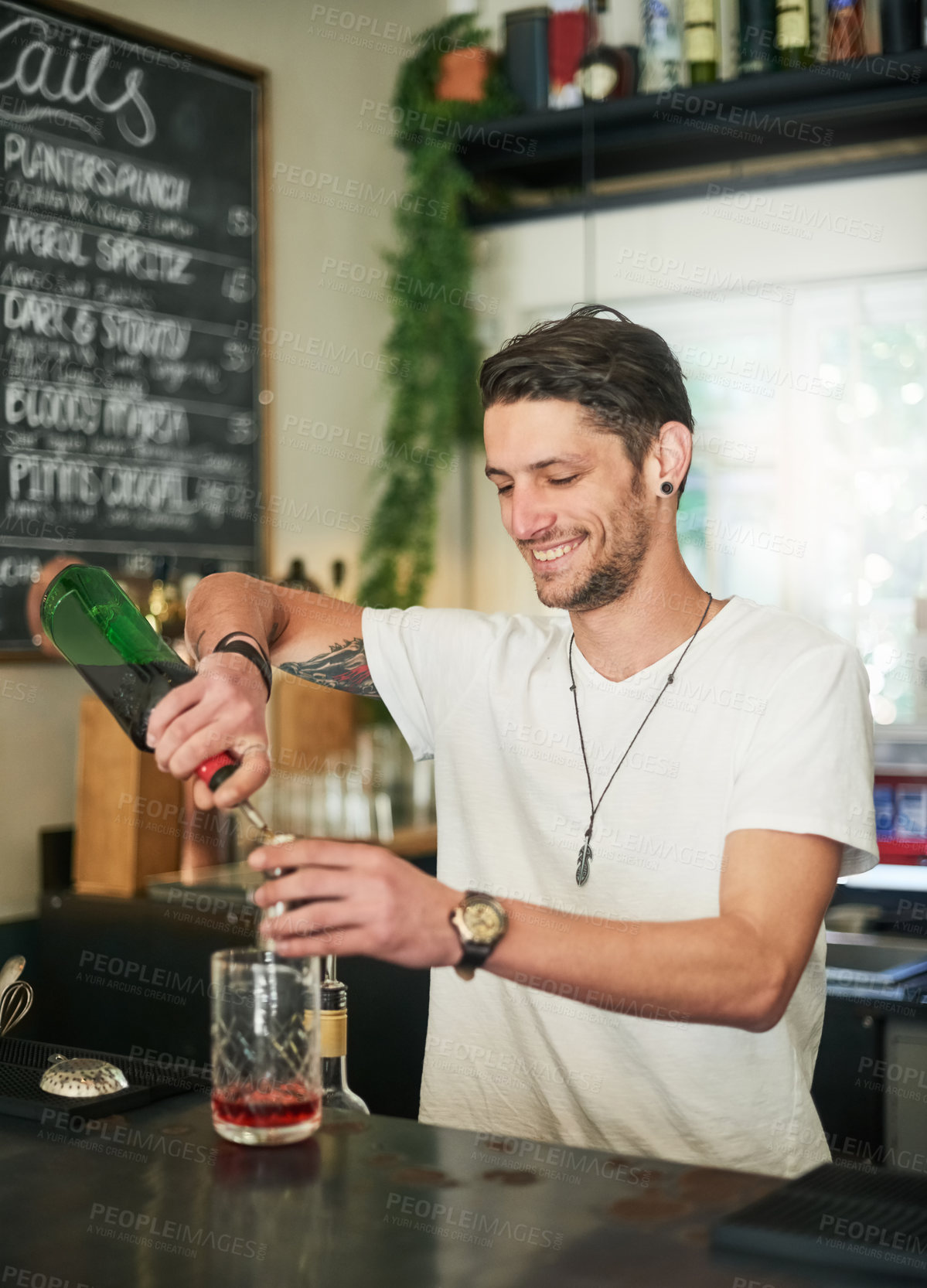 Buy stock photo Shot of a happy young bartender mixing a cocktail while standing behind the bar