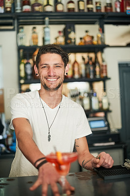 Buy stock photo Portrait of a happy young bartender serving a cocktail behind the bar