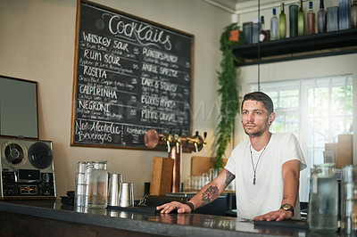 Buy stock photo Shot of a young bartender daydreaming while standing behind the bar