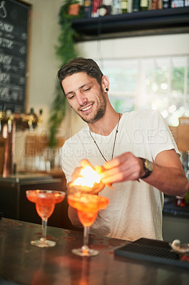 Buy stock photo Shot of a happy young bartender lighting a cocktail on fire behind the bar