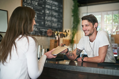 Buy stock photo Shot of a friendly young bartender helping a customer with her order across the bar counter
