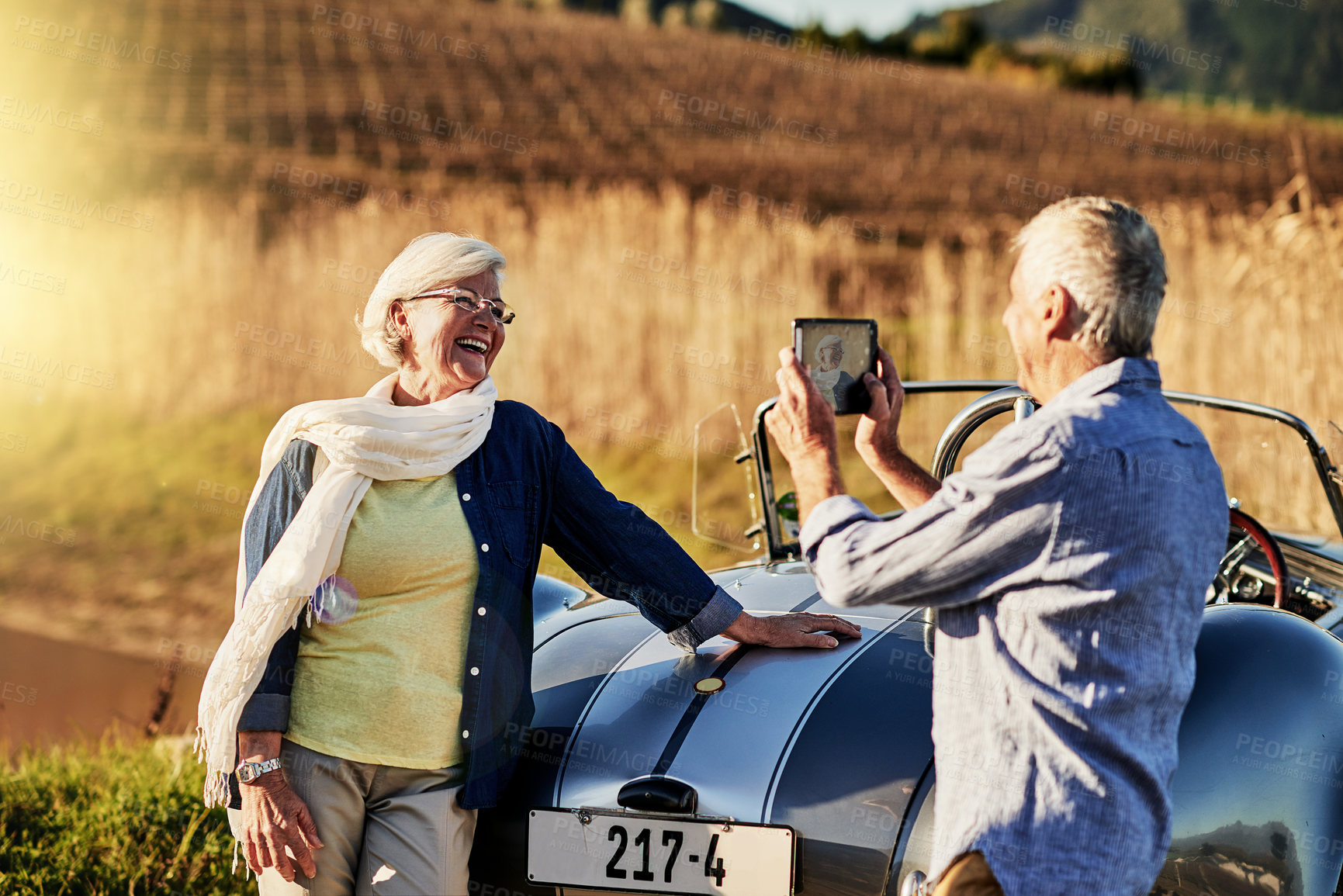 Buy stock photo Shot of a senior man taking  a picture of his wife while out on a roadtrip in a convertible