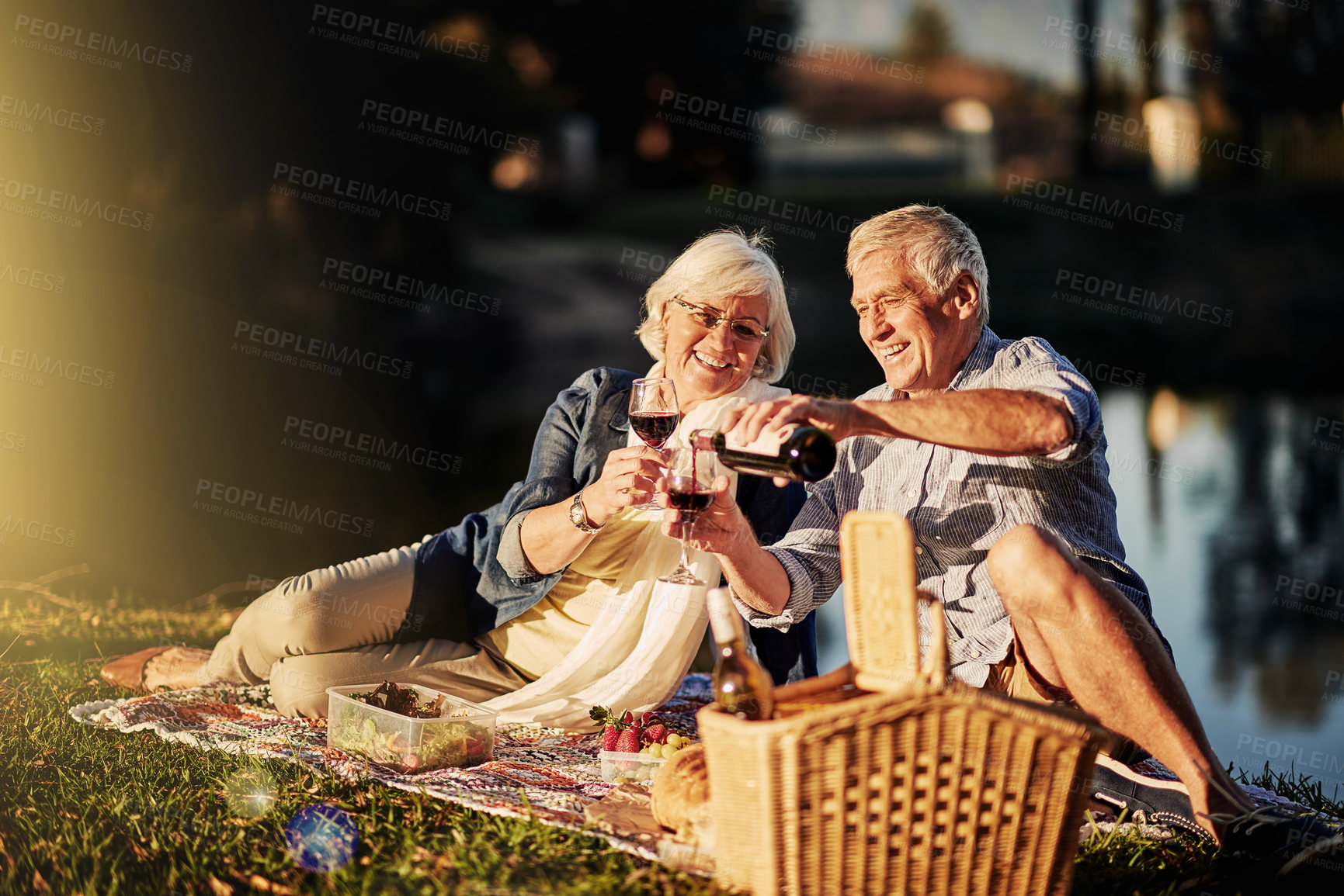 Buy stock photo Senior couple, talking and picnic in outdoor for wine, romance and relax by lake in nature. Elderly people, celebrate and drink alcohol on vacation, holiday and calm retirement for bonding by river