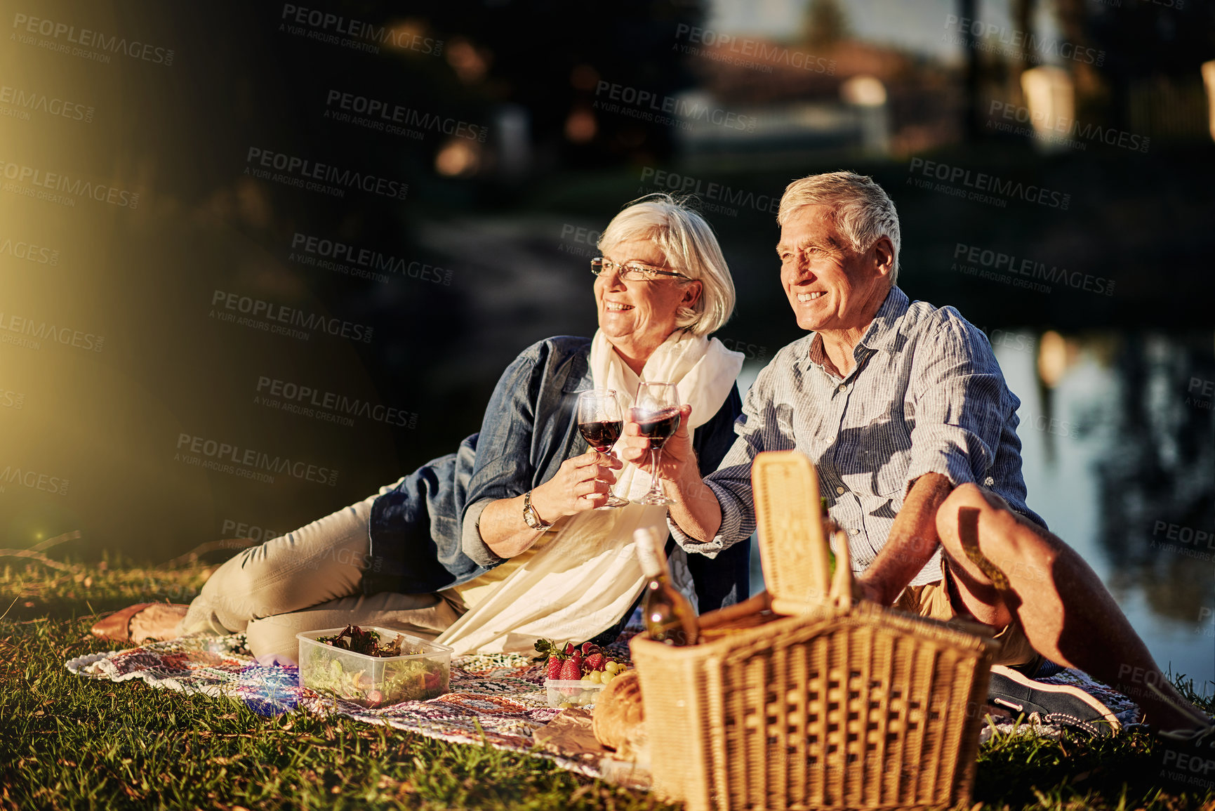 Buy stock photo Senior couple, picnic and toast outdoor for love, romance and relax by lake or nature. Elderly people, cheers and drink wine on vacation, holiday and calm celebration on anniversary by river
