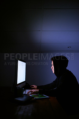 Buy stock photo Shot of a hooded computer hacker using a computer in the dark