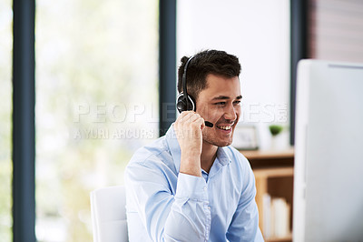 Buy stock photo Shot of a happy young man wearing a headset and using a computer at work