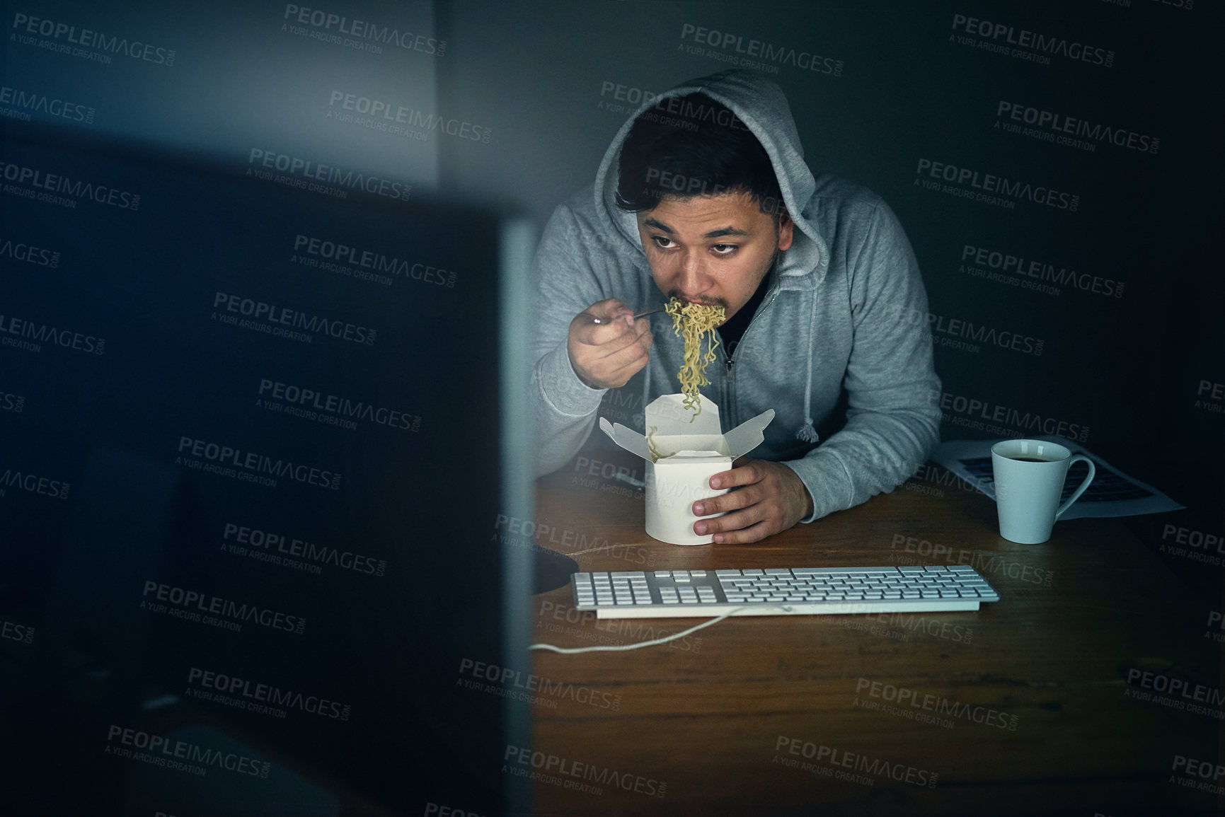 Buy stock photo Shot of a young man eating takeaway while working at his computer late in the evening