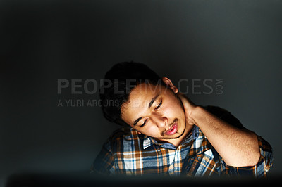 Buy stock photo Shot of a young designer massaging his sore neck while working on his computer late at night