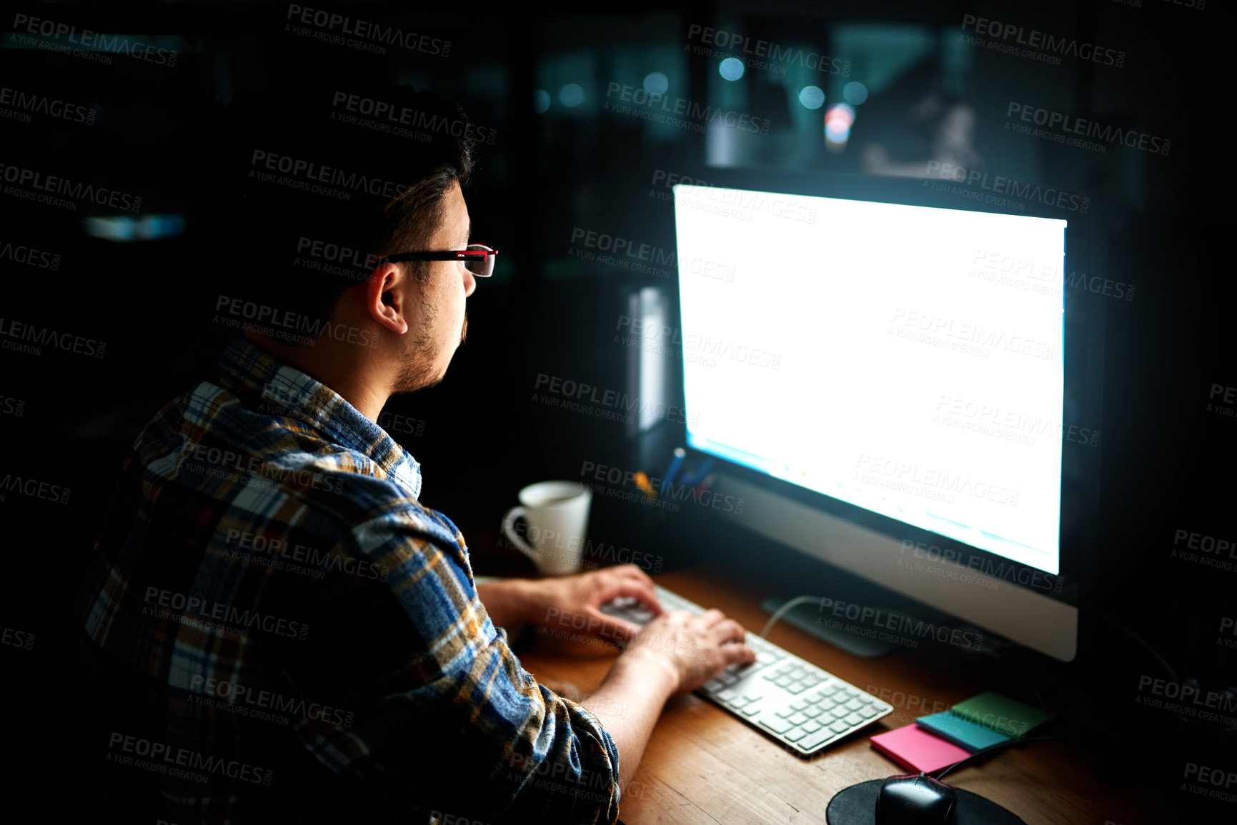 Buy stock photo Shot of a young male designer working on his computer late at night