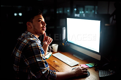 Buy stock photo Shot of a young male designer deep in thought whhile working on his computer late at night
