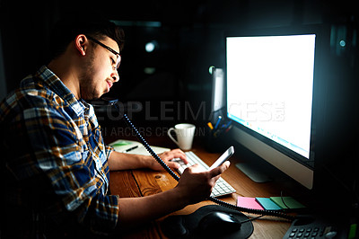Buy stock photo Shot of a designer reading a text message while working at his computer late in the evening