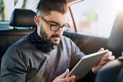 Buy stock photo Shot of a young designer using a digital tablet in a car
