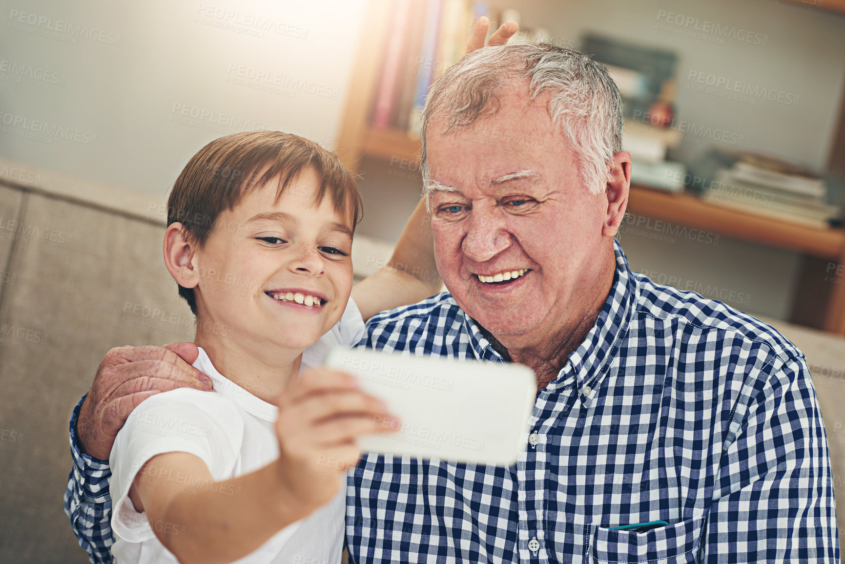 Buy stock photo Shot of a happy grandfather and his grandson taking a selfie together on a mobile phone at home