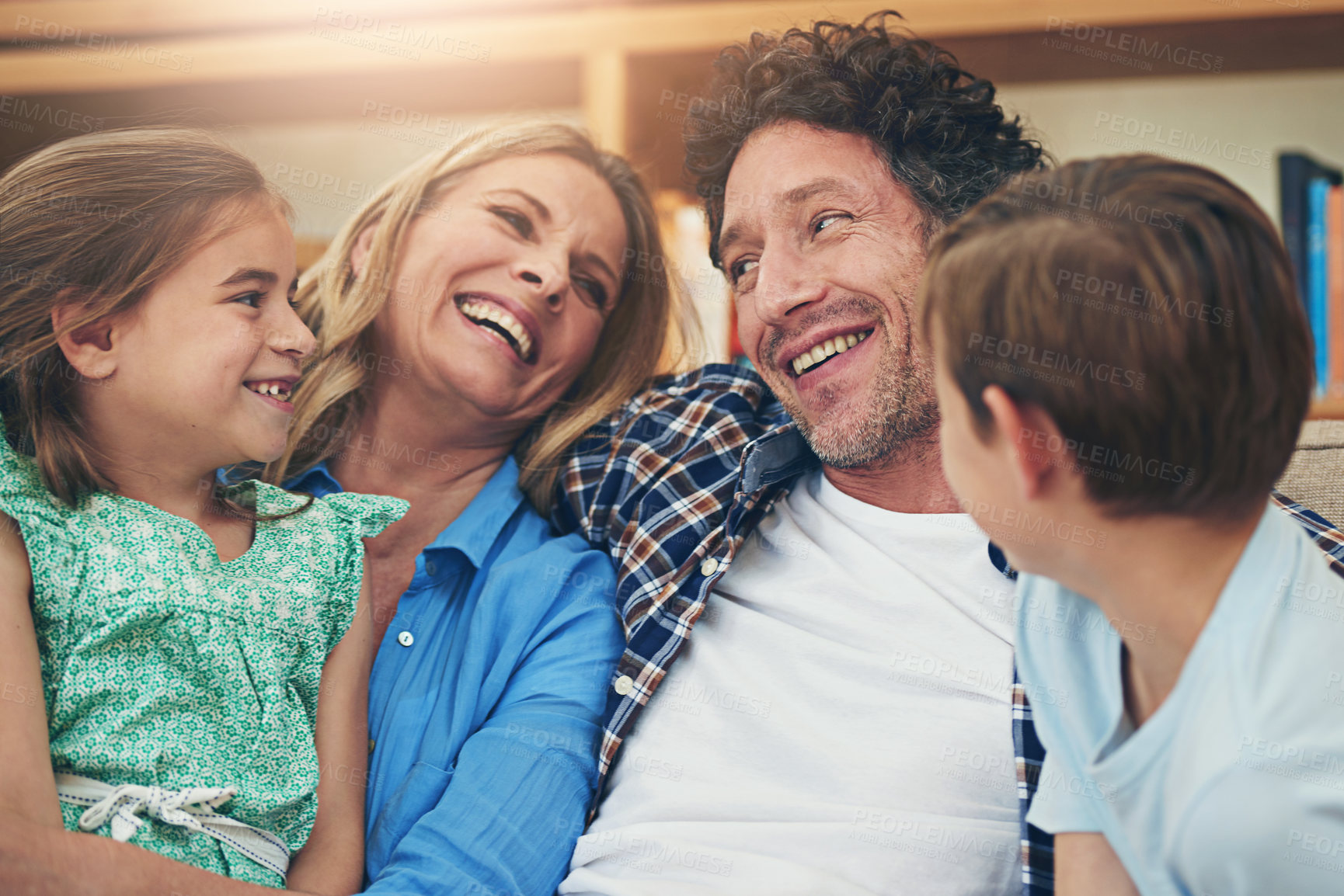 Buy stock photo Laughing, parents and children on sofa for love, playing and bonding together in living room. Lens flare, mother and father with kids on couch for embrace, happiness or weekend break in home