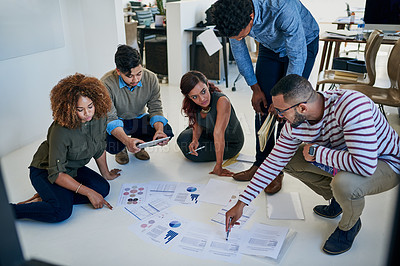Buy stock photo Shot of colleagues going through paperwork together on the floor in a modern office
