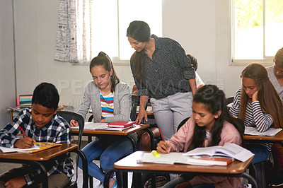 Buy stock photo Shot of a young teacher helping her students with their homework in class