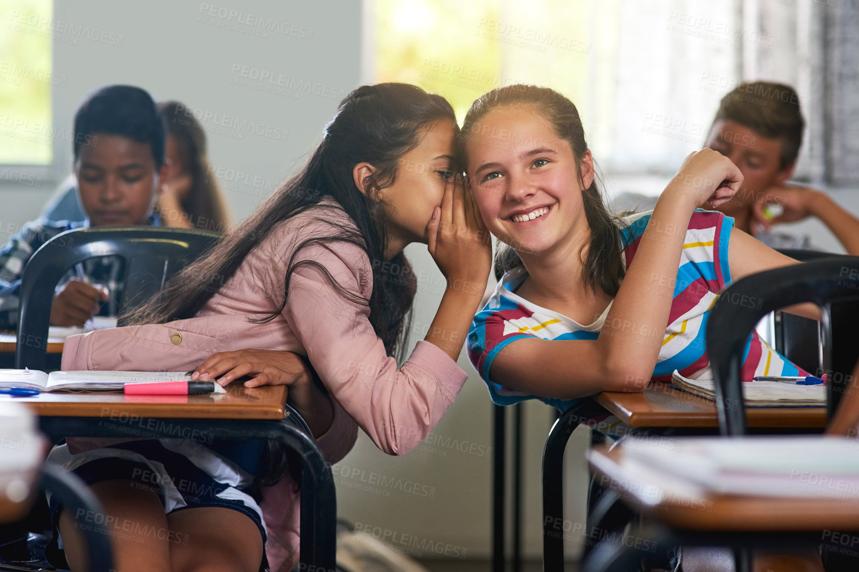 Buy stock photo School, friends and whisper in classroom for secret, story and gossip together with hand by desk. Campus, students and girls talking in ear in class for news, info and chat  with private discussion