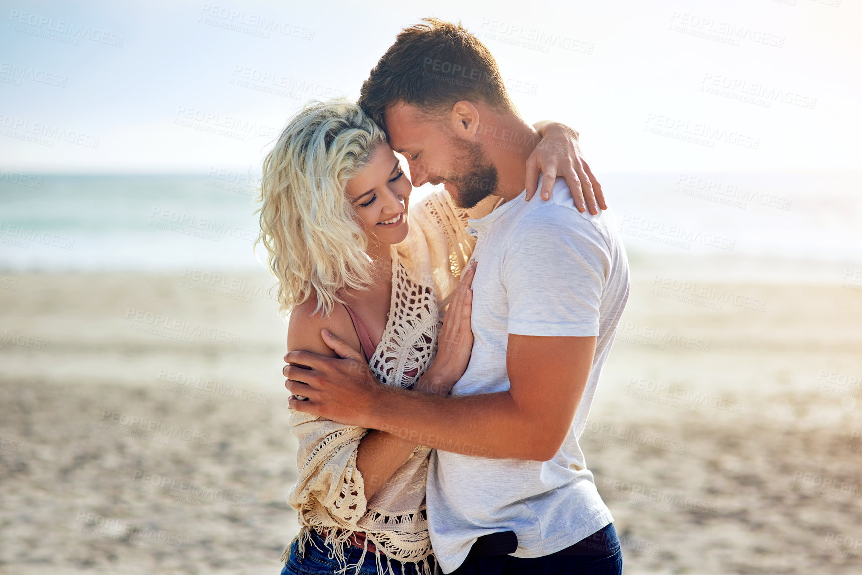 Buy stock photo Smile, couple and hug by ocean with love for seaside romance, serene seascape and beach view with affection. Man, woman and together for bonding by coast on weekend date, embrace and break with care.