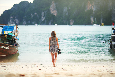 Buy stock photo Rear view shot of a young woman walking on the beach with a camera in hand