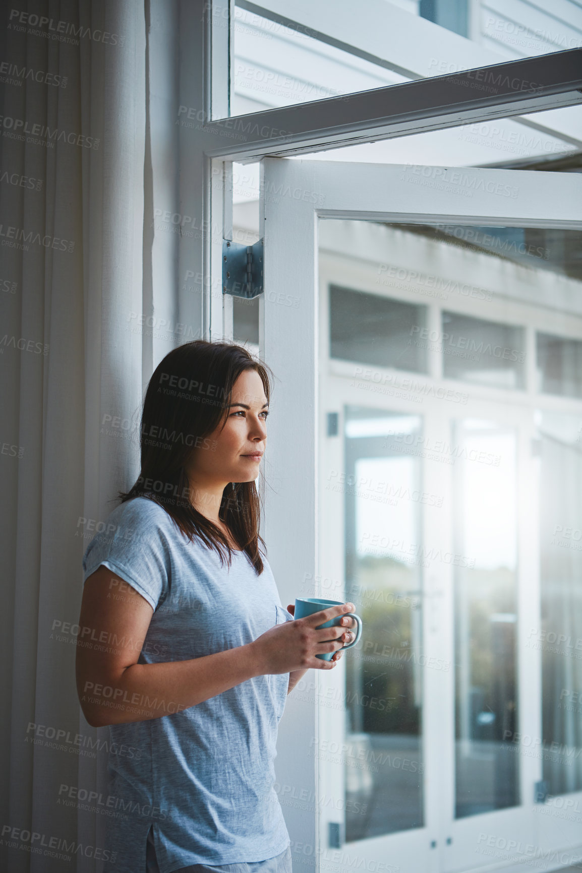 Buy stock photo Cropped shot of an attractive young woman enjoying a coffee by her patio door