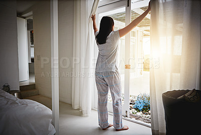 Buy stock photo Rearview shot of an attractive young woman opening up the curtains over her patio door
