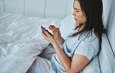 Buy stock photo High angle shot of an attractive young woman reading her text messages while lying in bed