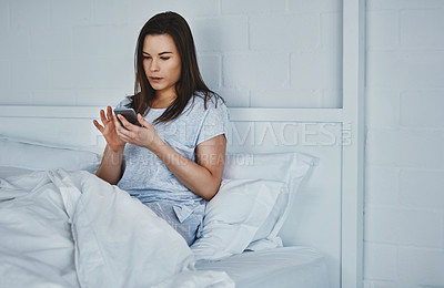 Buy stock photo Cropped shot of an attractive young woman reading her text messages while lying in bed