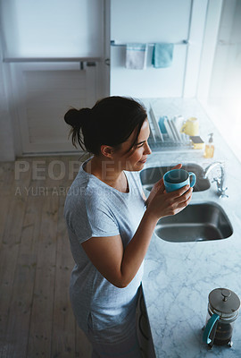Buy stock photo High angle shot of an attractive young woman enjoying a coffee while standing in the kitchen