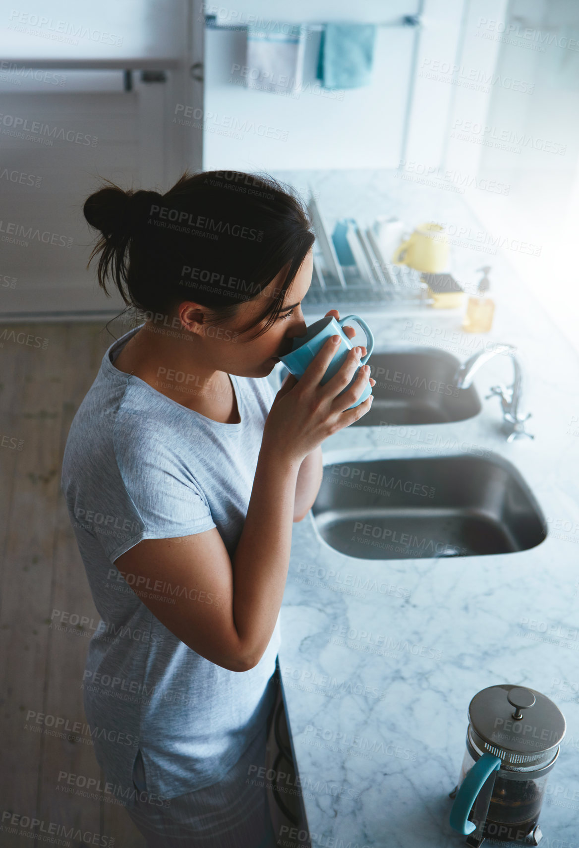 Buy stock photo High angle shot of an attractive young woman enjoying a coffee while standing in the kitchen