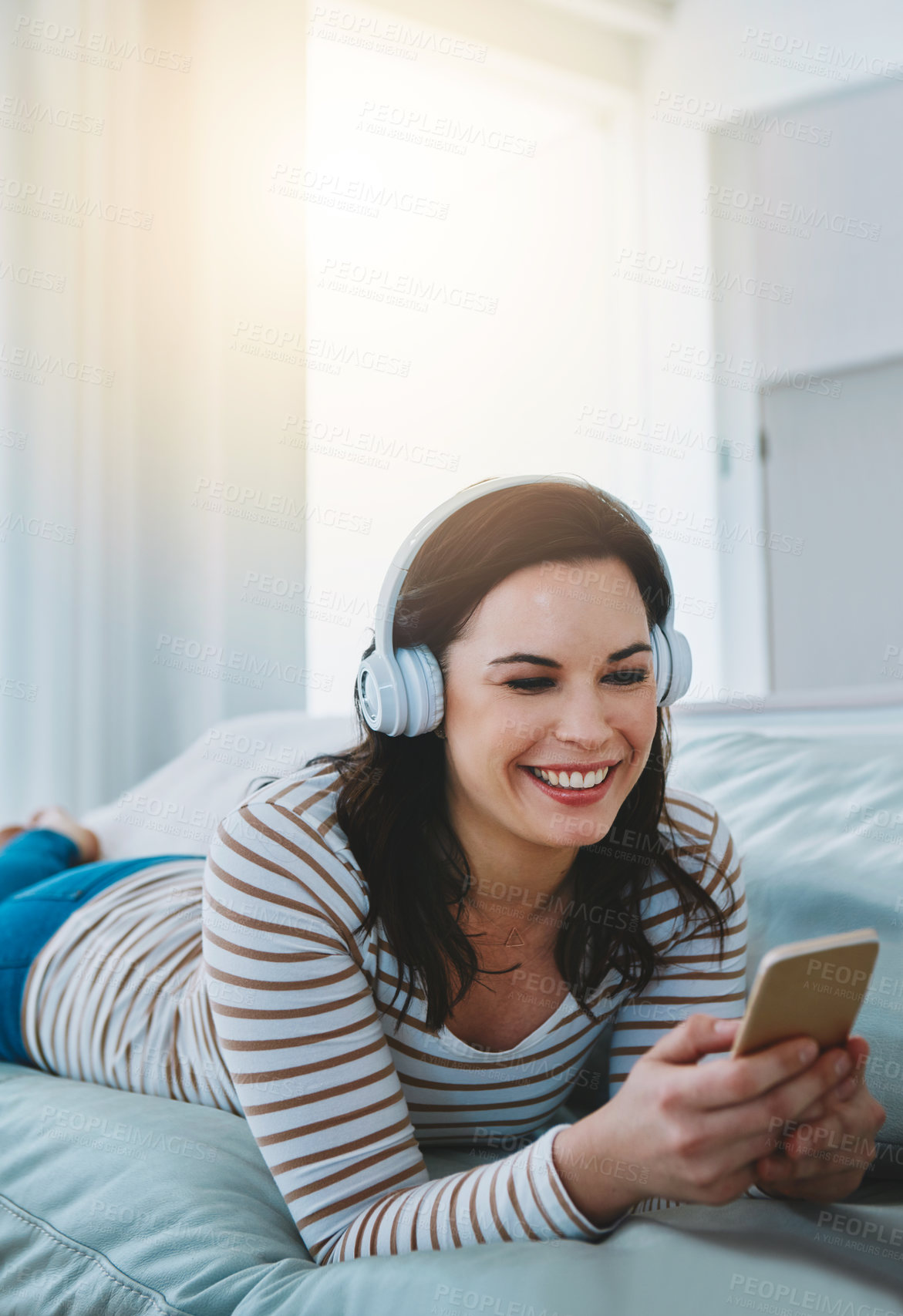 Buy stock photo Shot of a young woman relaxing on the sofa and using her phone and headphones