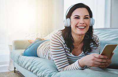 Buy stock photo Shot of a young woman relaxing on the sofa and using her phone and headphones