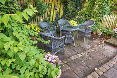 Buy stock photo Rattan chairs around a table in a lush garden patio on a bright and sunny day. Rustic outdoor furniture in a calm and peaceful environment surrounded by nature in spring. Cosy spot to enjoy a picnic
