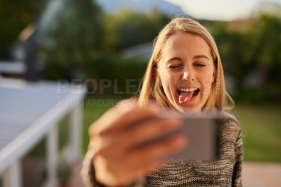 Buy stock photo Cropped shot of an attractive young woman sticking her tongue out while taking a selfie outside