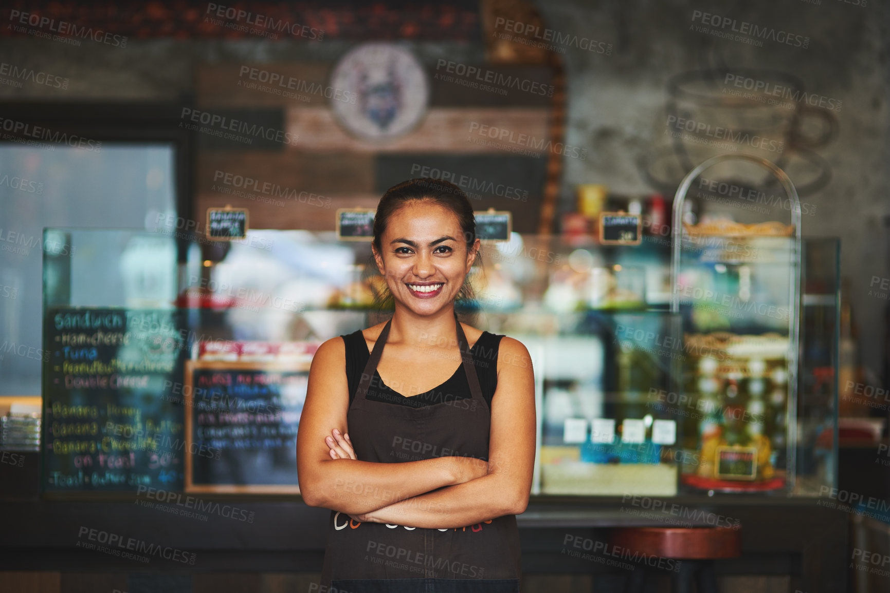 Buy stock photo Portrait of a young barista posing with her arms crossed in a coffee shot